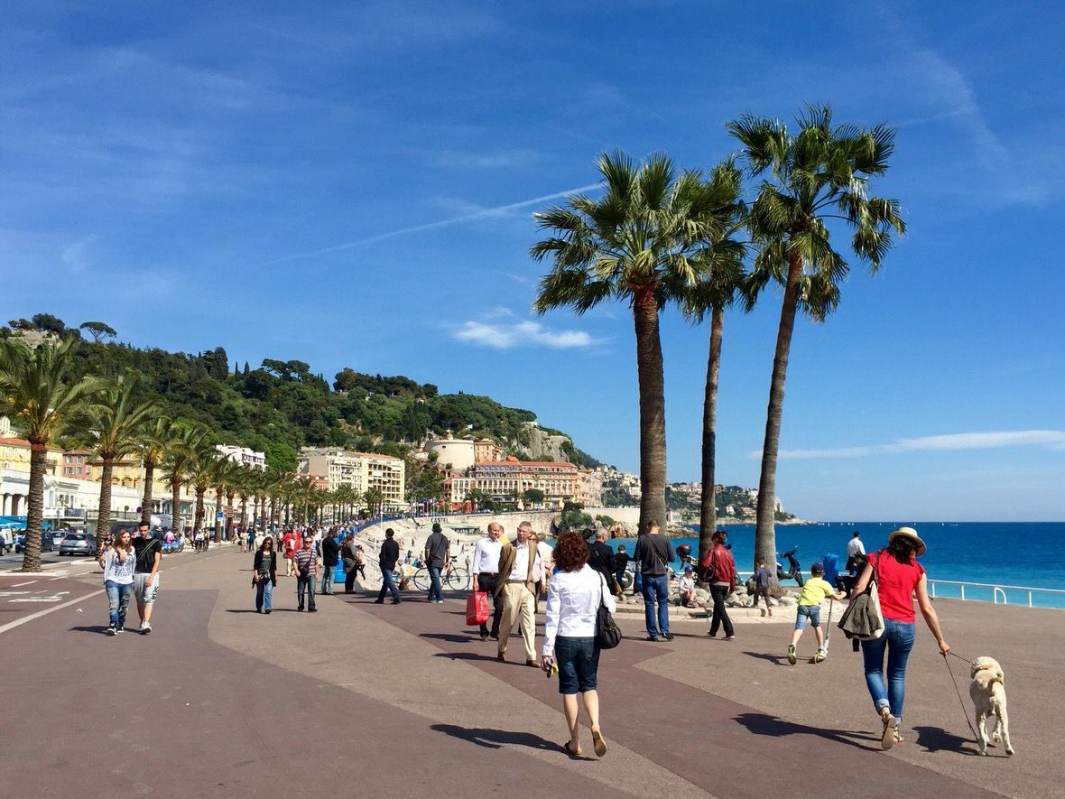 Coastal promenade with palm trees, people strolling, blue sea and sky. The French Riviera The French Riviera Nice