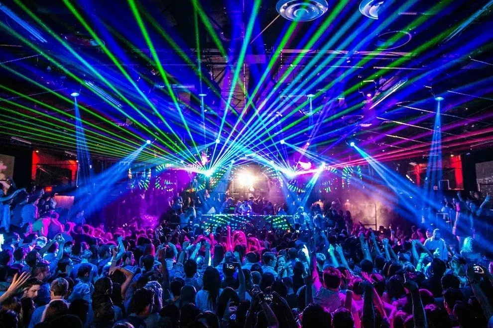 A packed dance floor with a DJ, bathed in colorful laser beams, blue, green, and pink lights. Phillipines Manilaa
