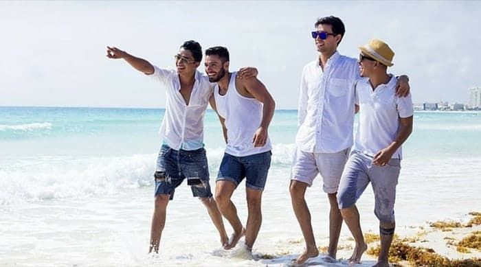 Four men walking on a beach, one pointing, wearing light-colored shirts and shorts; sunny day. Puerto Rico