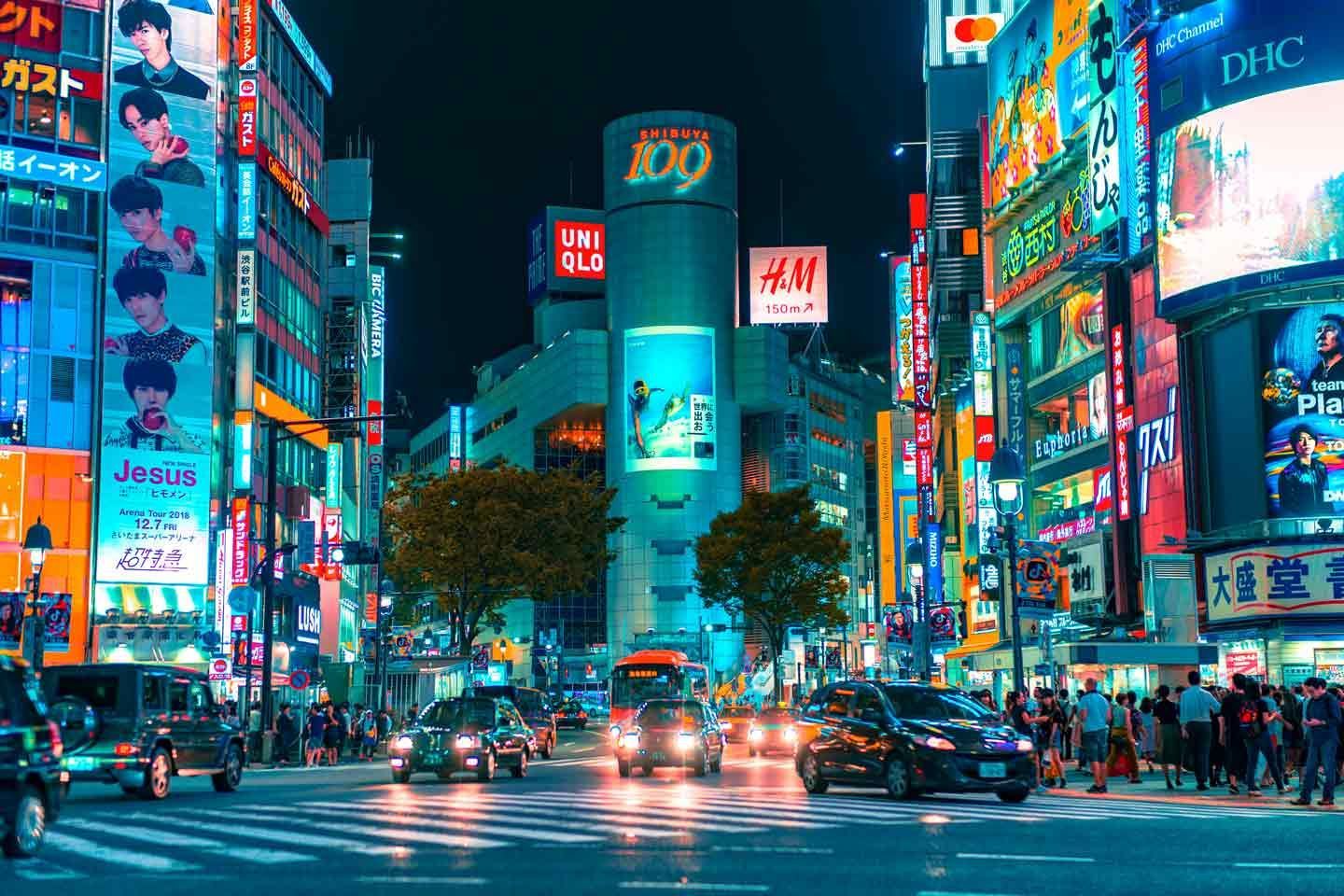 Nighttime view of Shibuya crossing in Tokyo, Japan, with neon signs, cars, and pedestrians.