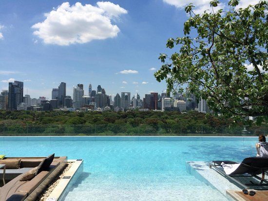 Infinity pool overlooking a city skyline. Blue water, sunny sky, trees, and lounging chairs.
