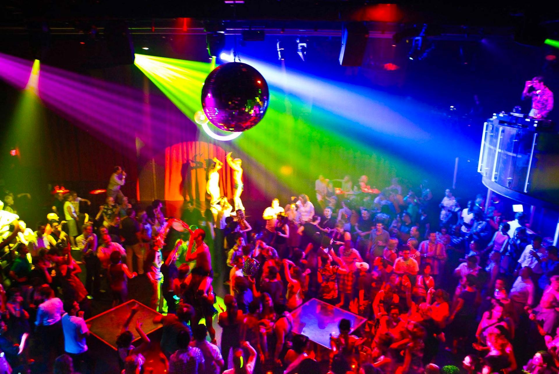 A crowded nightclub with a disco ball, colorful lights, and people dancing and socialising. Thailand Gay Night Club