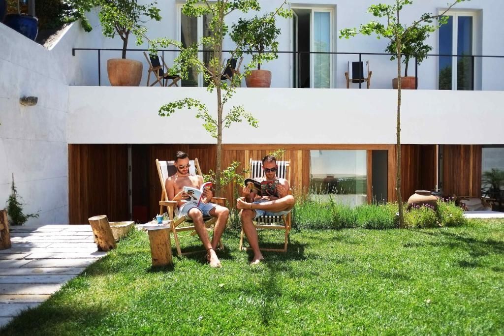 Two people relaxing in lawn chairs, reading magazines, with a dog, outside a modern white building. The Late Birds Lisbon