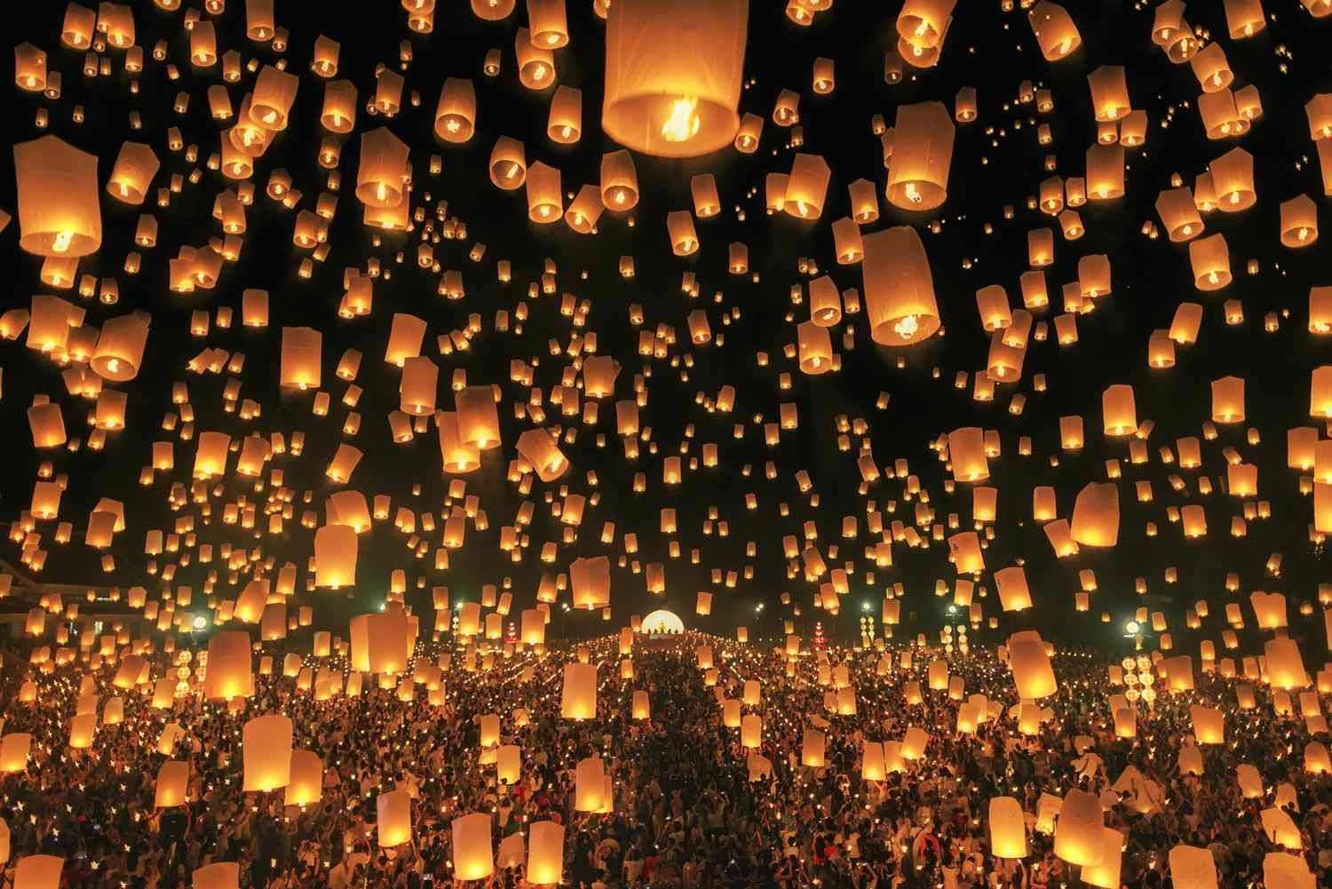 Thousands of illuminated paper lanterns float in the night sky above a large crowd. Thailand