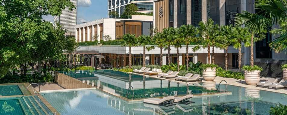 Pool area with lounge chairs, trees, and buildings in the background.