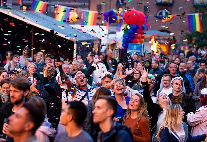 Large crowd celebrating outdoors, rainbow flags and confetti. People cheering, looking up with joyful expressions. Copenhagen – Cool, Progressive