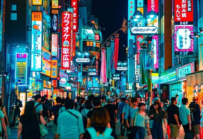 Gay Nighttime street scene in a crowded area of Tokyo, Japan, filled with neon signs and people walking.