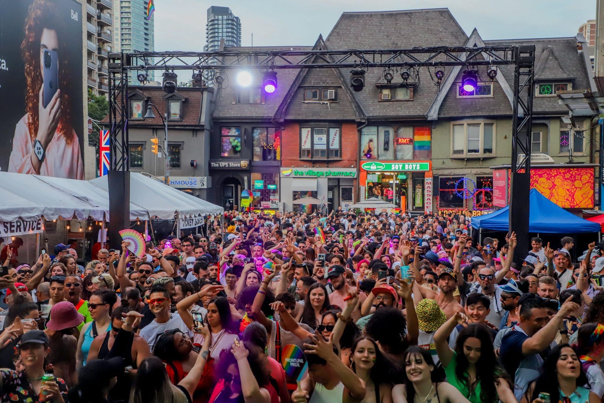 A large crowd dances at a street festival with a stage, colorful buildings, and rainbow flags in the background.Toronto Pride Festival (Canada)