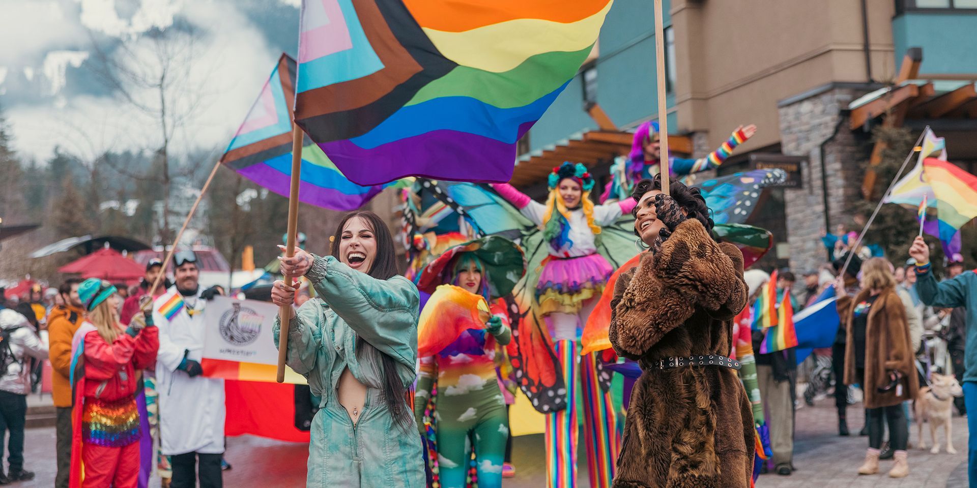 People holding Pride flags at a parade. Some are in costume. The setting is outdoors in a town.