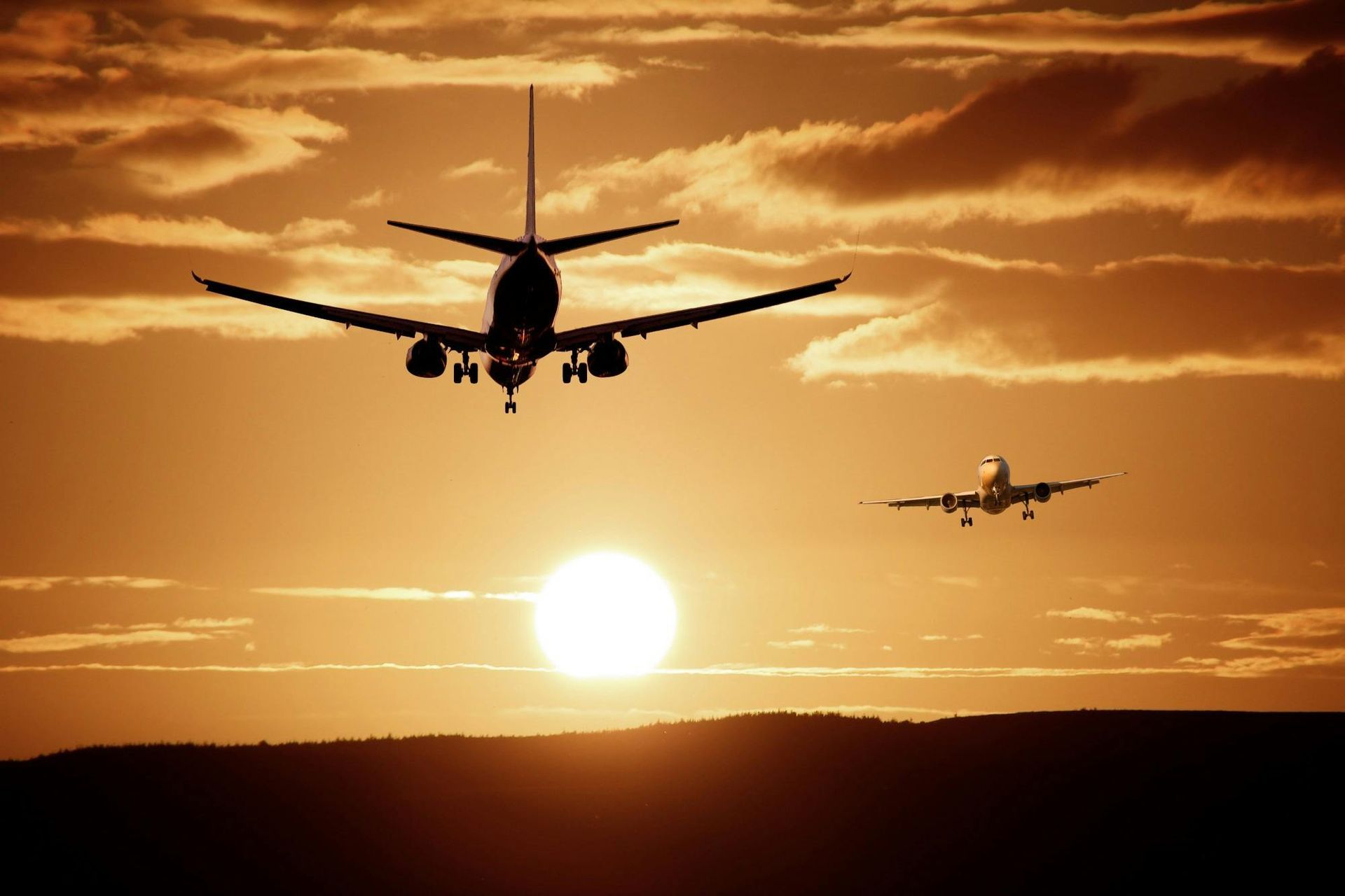 Two airplanes silhouetted against a golden sunset, one larger, descending, and one smaller in the distance.
