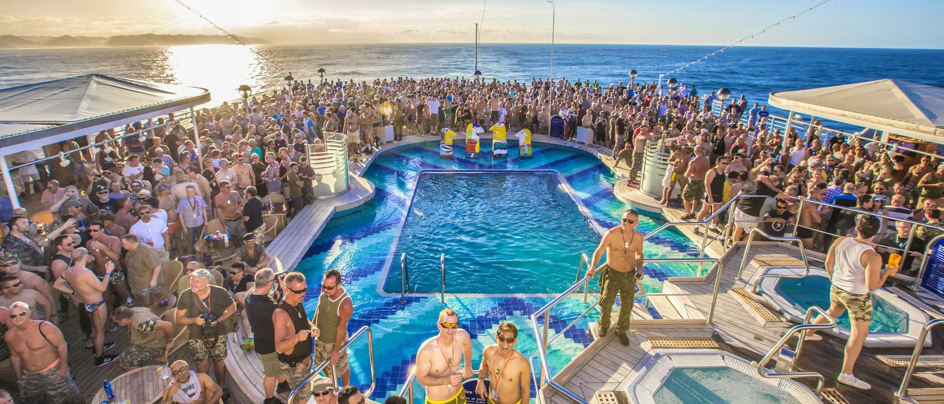 Large crowd around a pool on a ship at sea. People are in and around the water.