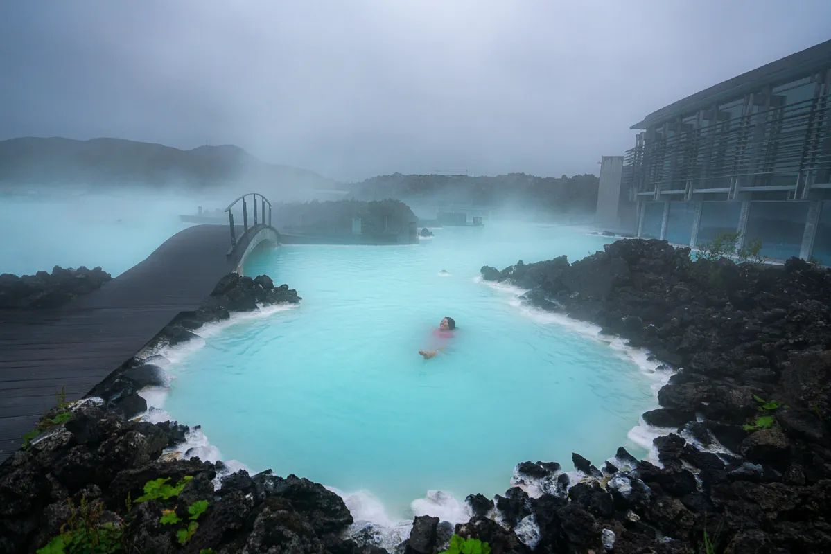 A person swims in the bright blue geothermal water of the Blue Lagoon in Iceland.