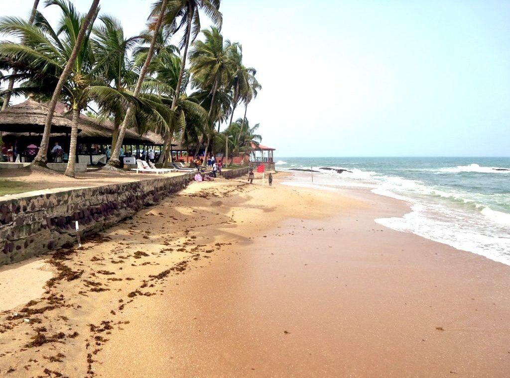 Sandy beach with palm trees, a restaurant, and the ocean under a clear sky. Cape Coast, Ghana