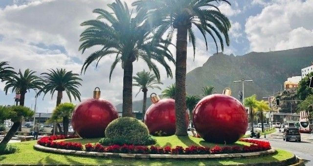 Giant red Christmas ornaments in a roundabout with palm trees, with mountains in the background.  Gran Canaria