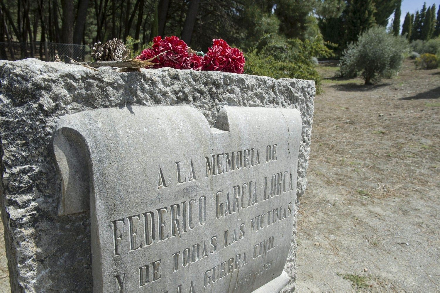 Memorial stone for Federico García Lorca with red flowers on top, outdoors.