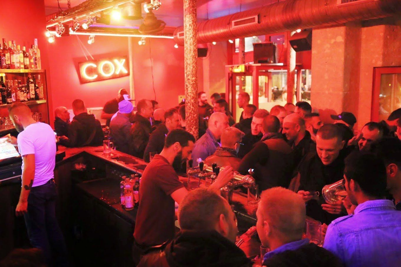 Inside a crowded bar, red lighting. Sign says