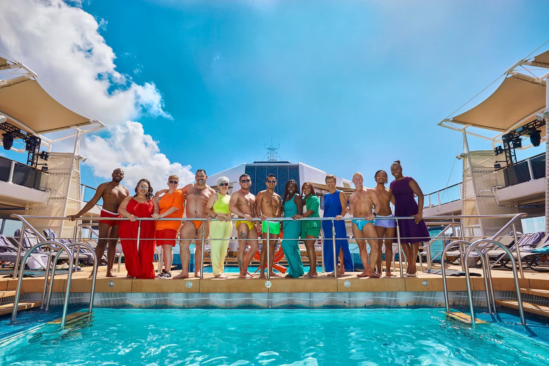 Group of people in colorful outfits posing by a pool on a sunny cruise ship deck.