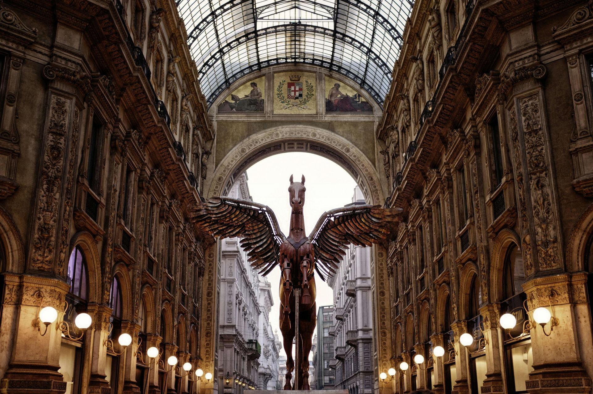 A bronze Pegasus sculpture stands in a covered, arched shopping arcade in Milan, Italy.