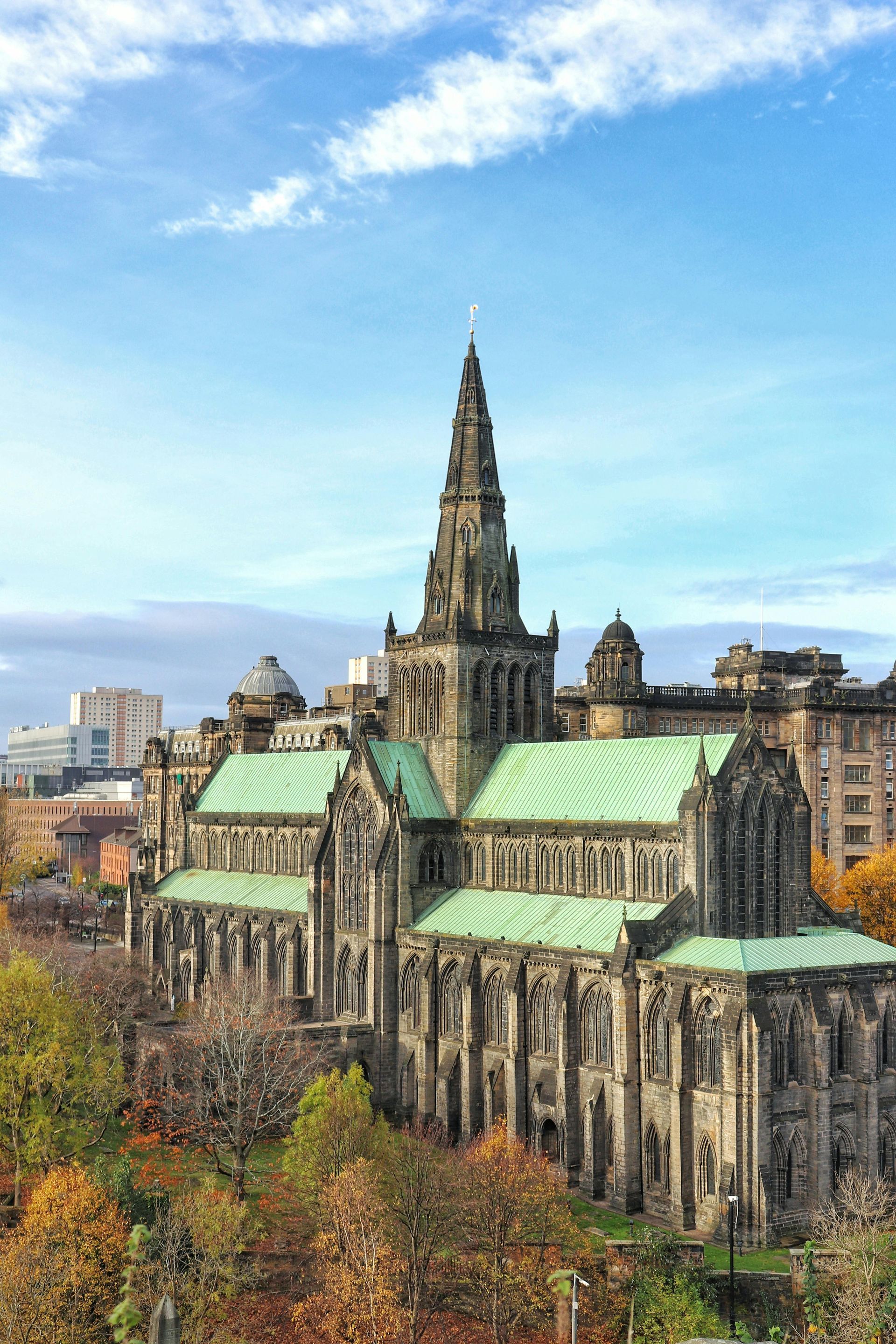 Gothic cathedral with green copper roofs and tall spire above autumn trees under a blue sky