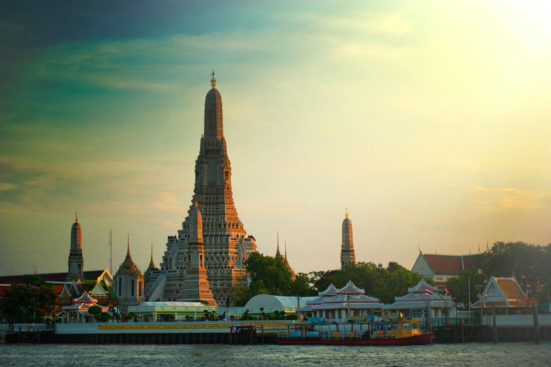 Wat Arun temple, Bangkok, Thailand, with ornate spires at sunset, reflecting in the river.