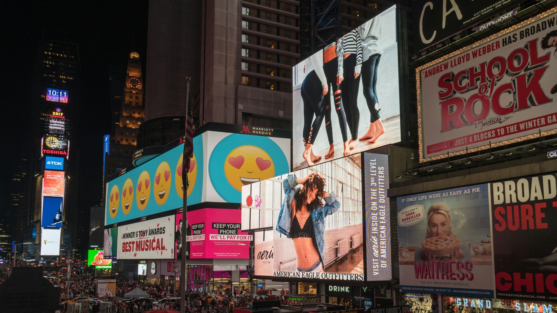 Times Square at night, brightly lit billboards, crowds below.