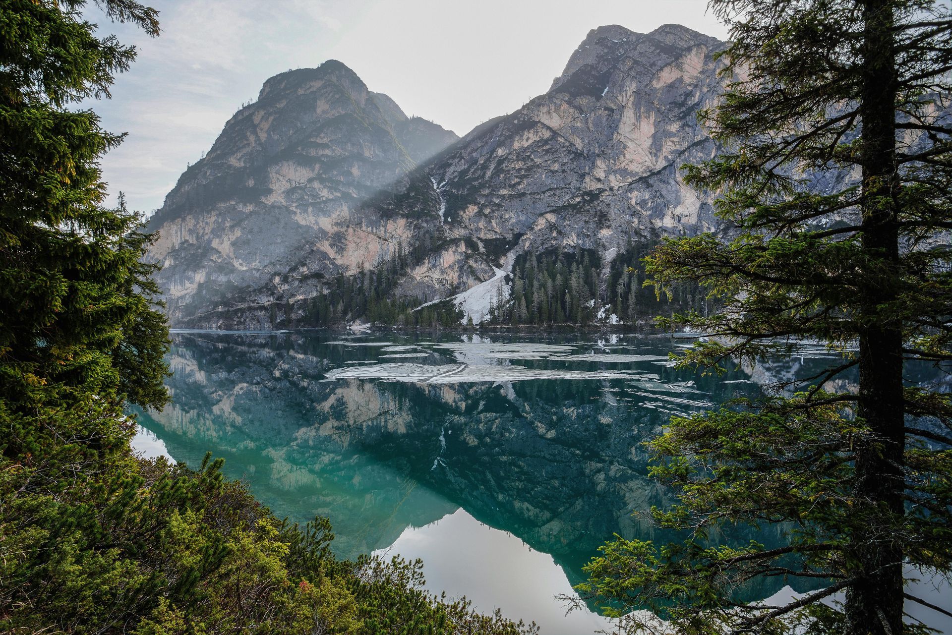 Mountains reflected in a turquoise lake framed by trees. Snowy peaks, a clear sky.