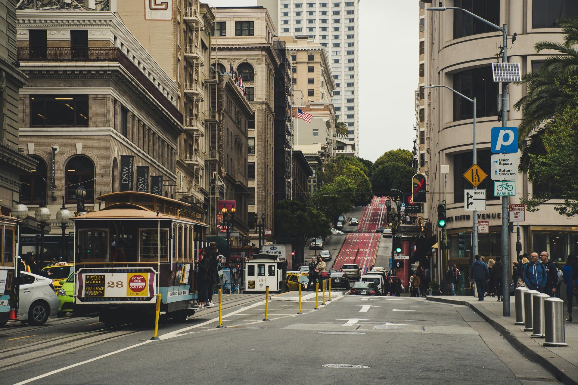 Cable car on a San Francisco street with tall buildings and a steep red-painted hill in the background.