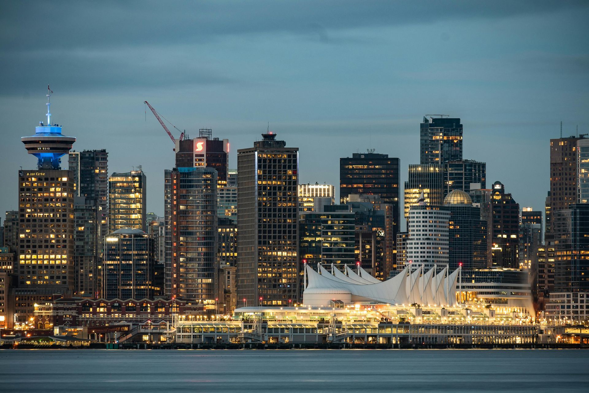 Downtown Vancouver skyline at dusk, lights reflecting on water.