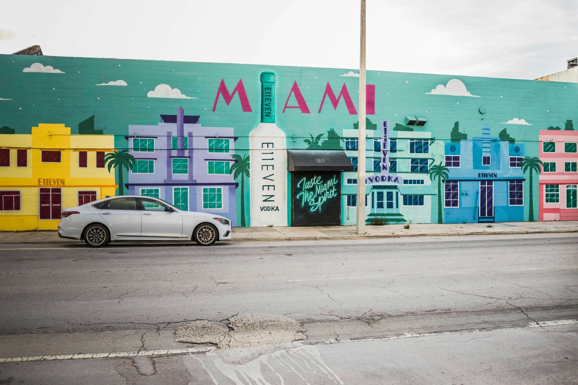 Silver car parked in front of a colorful Miami mural featuring buildings, the word