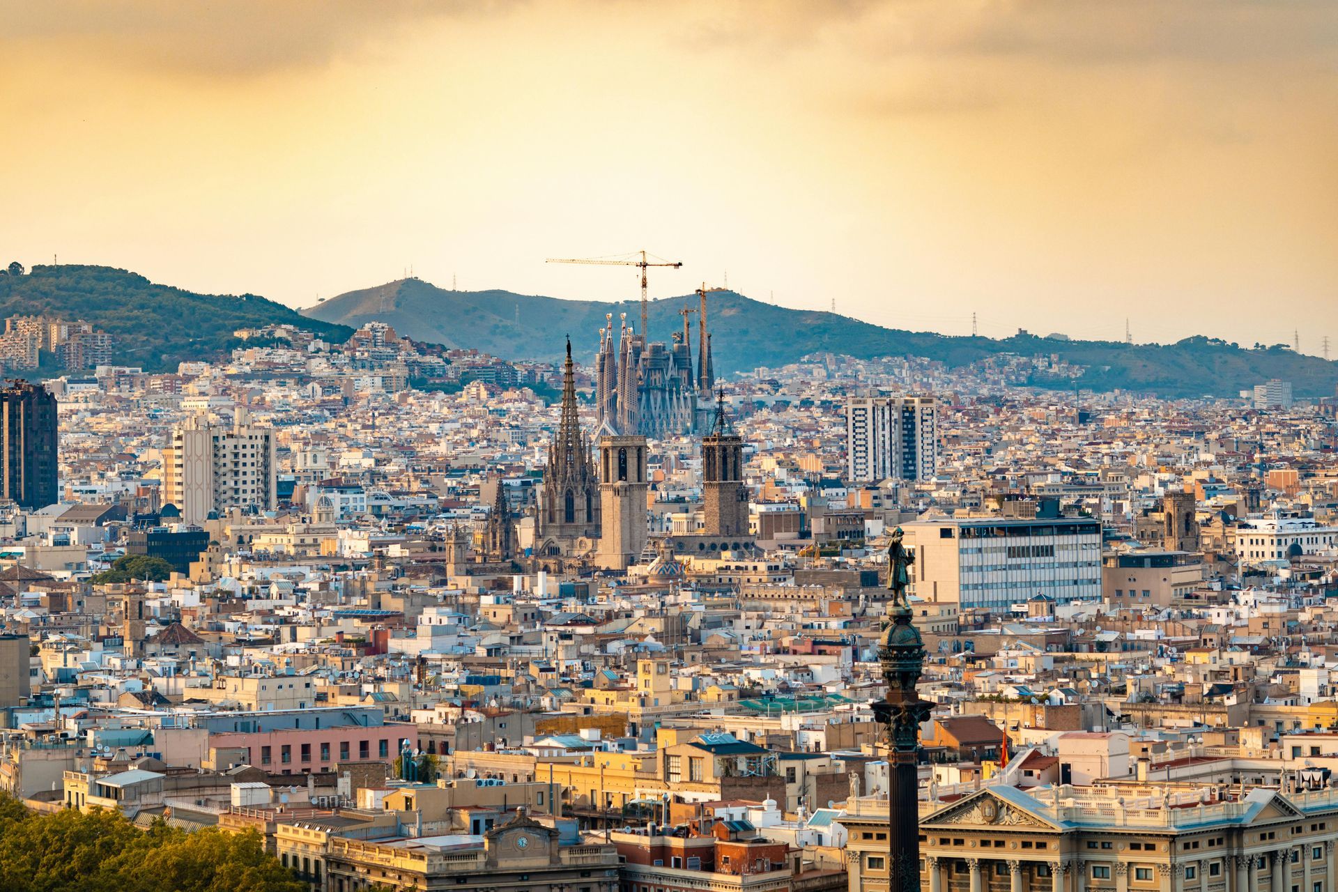Barcelona cityscape with the Sagrada FamĂlia at center under a warm, cloudy sky.