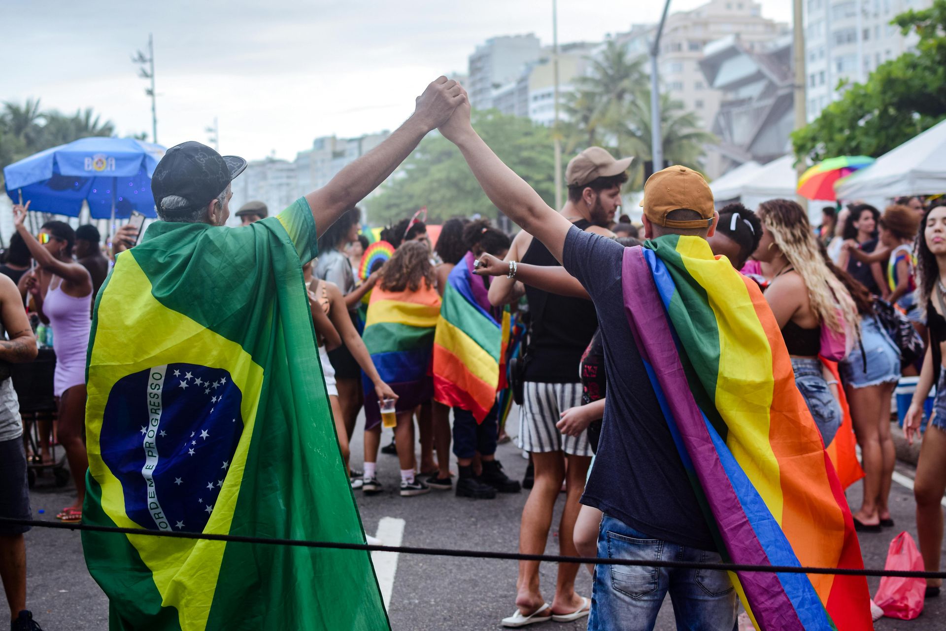 People at a Pride parade in Rio de Janeiro, with rainbow and Brazilian flags.