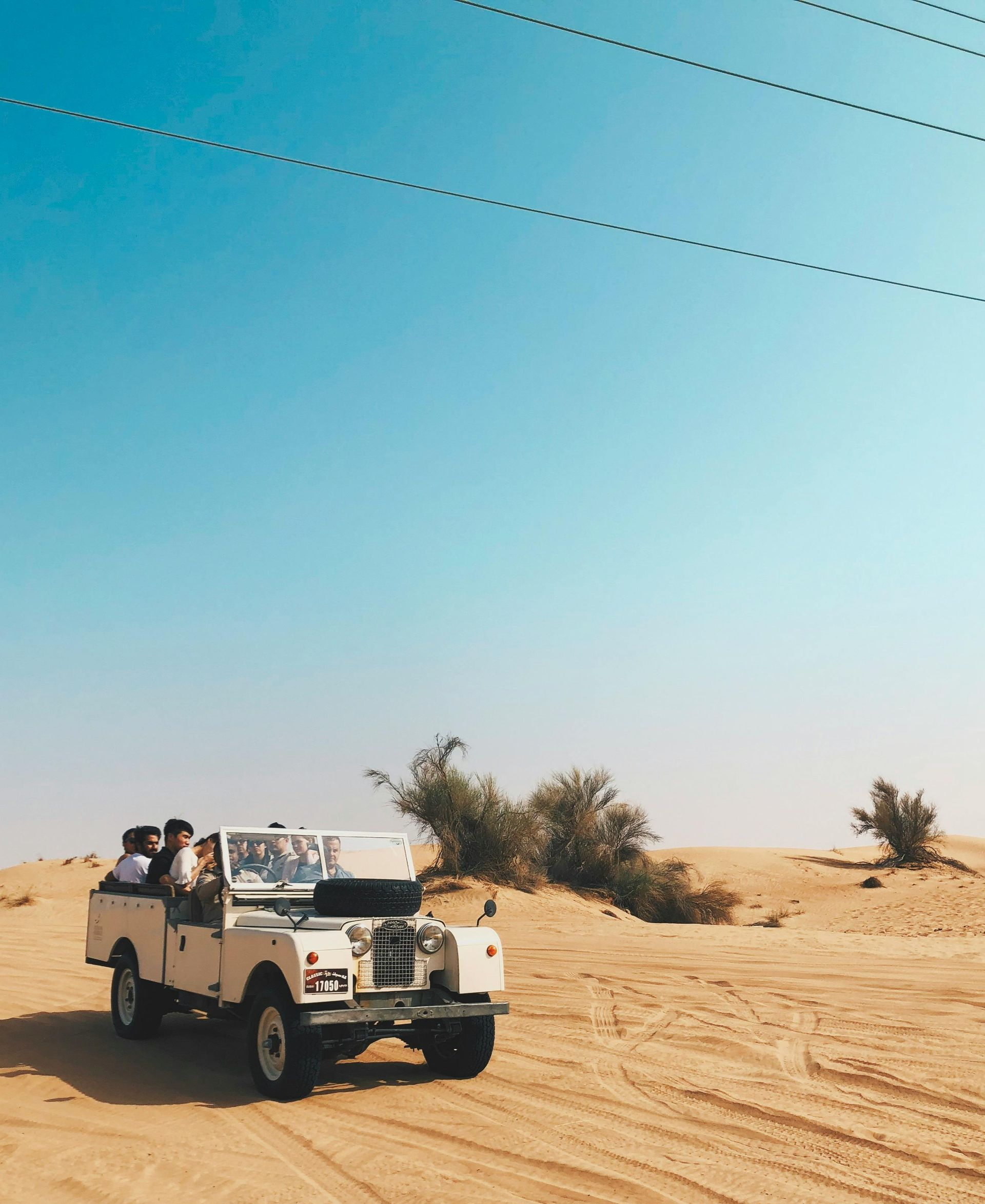 White jeep driving through a sandy desert on a bright, sunny day.