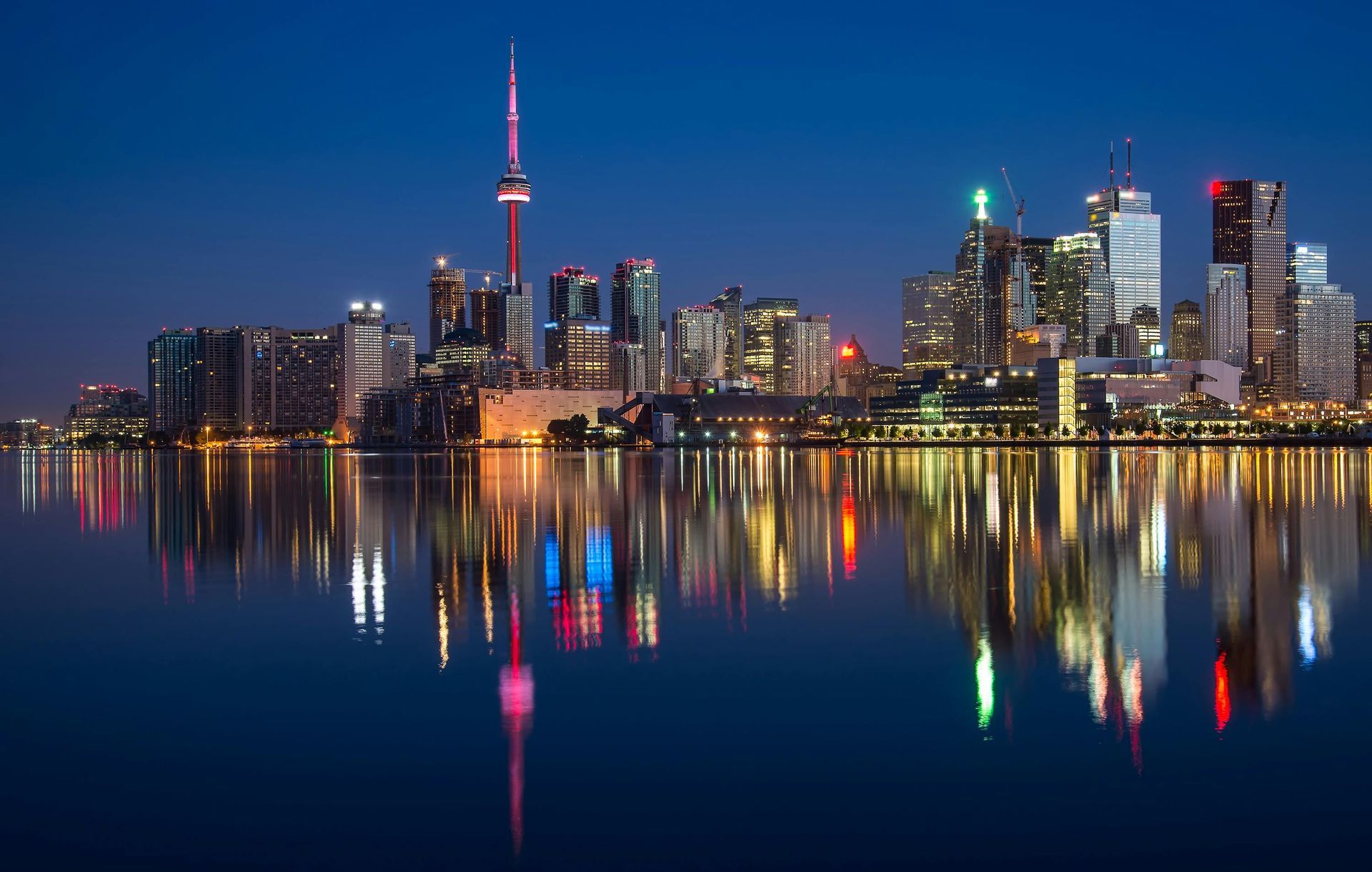 Toronto skyline at night, reflected in water. CN Tower prominent, city lights twinkle.