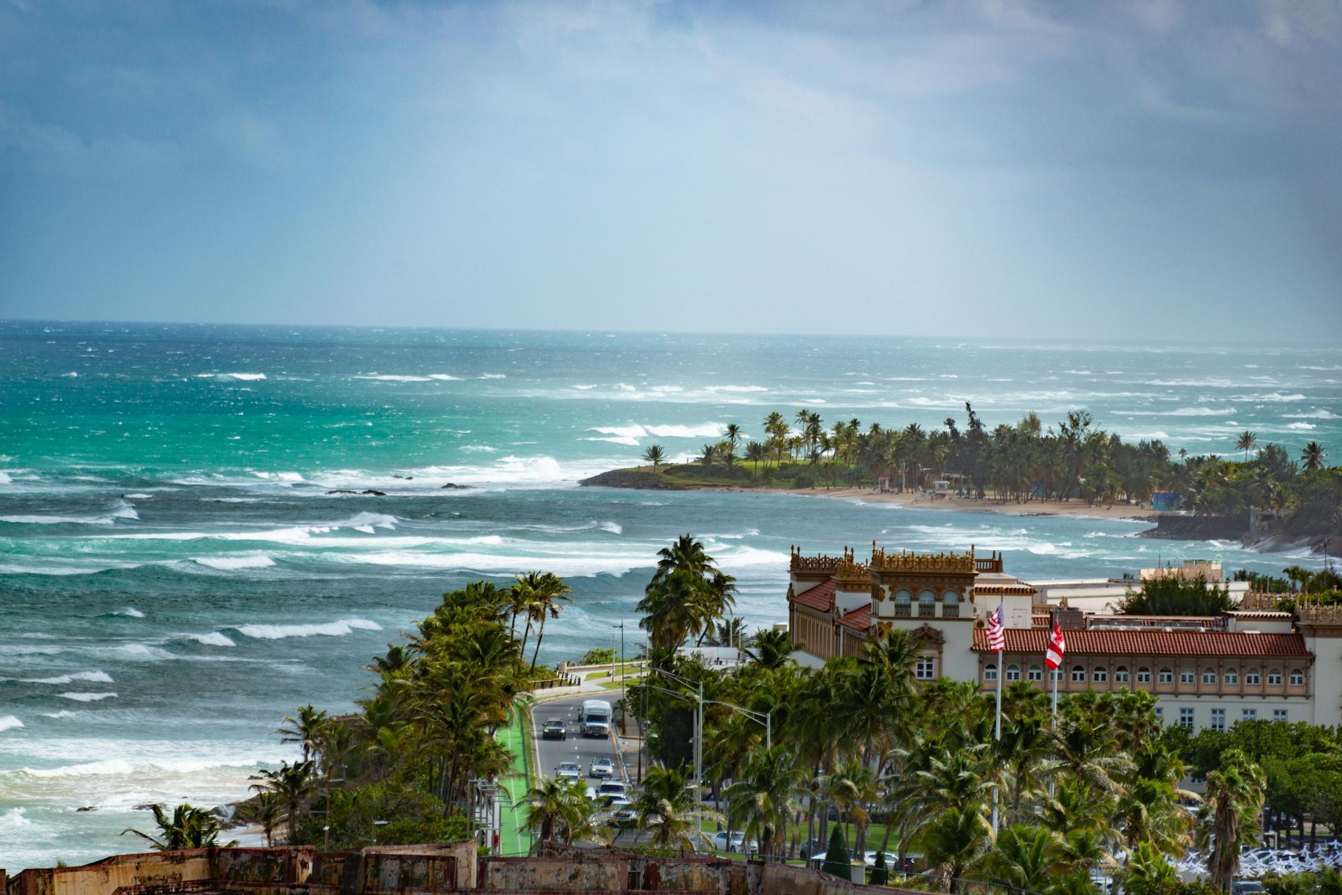 Coastal resort with palm trees, red-roofed buildings, and turquoise ocean Puerto Rico waves under a hazy sky