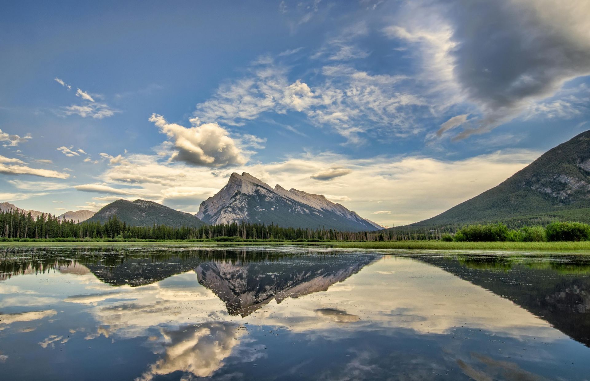 Mountain range reflected in calm lake under cloudy blue sky.