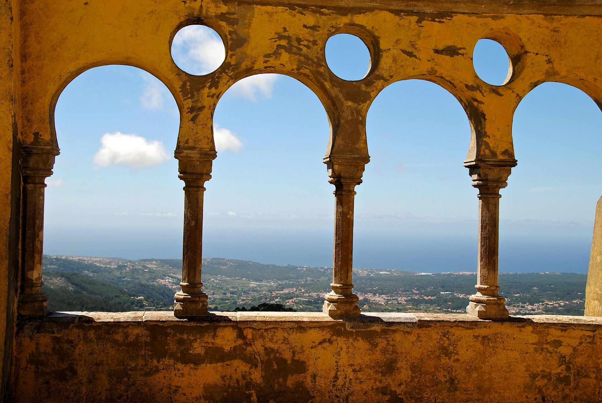 Arched yellow columns framing a view of blue sky, ocean, and distant green hills.