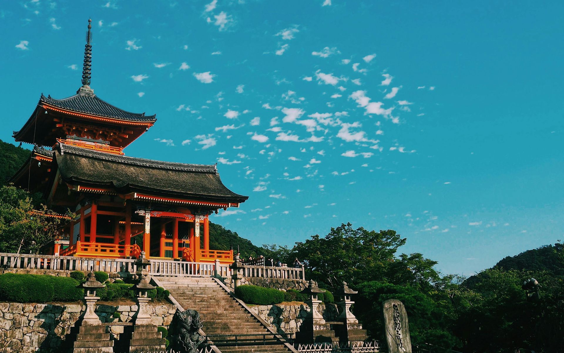 Orange and dark-roofed Japanese temple under a bright blue sky, stone steps leading up.