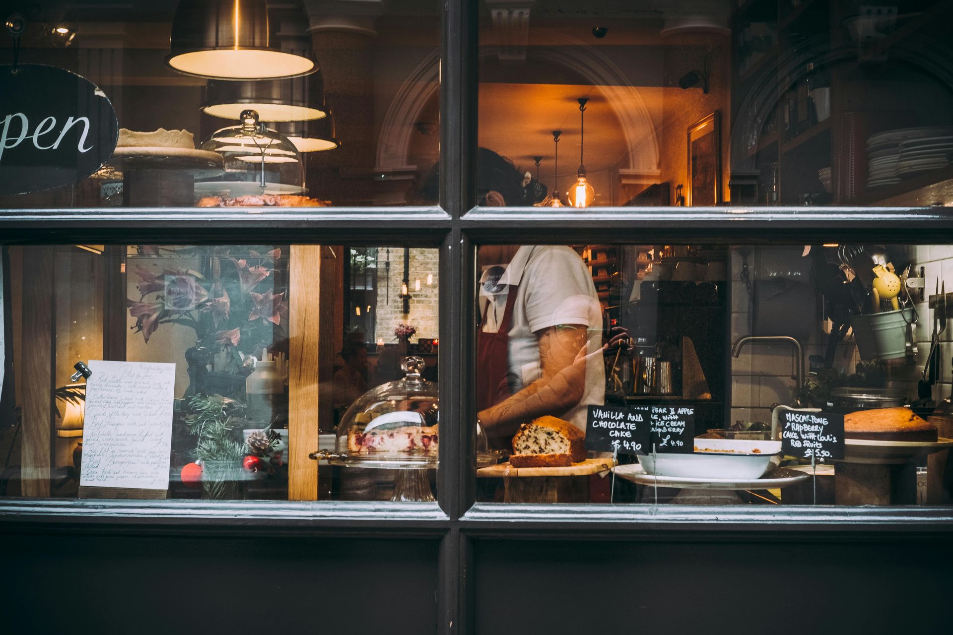 A cafe storefront with a person behind the counter, baked goods, and a sign that reads