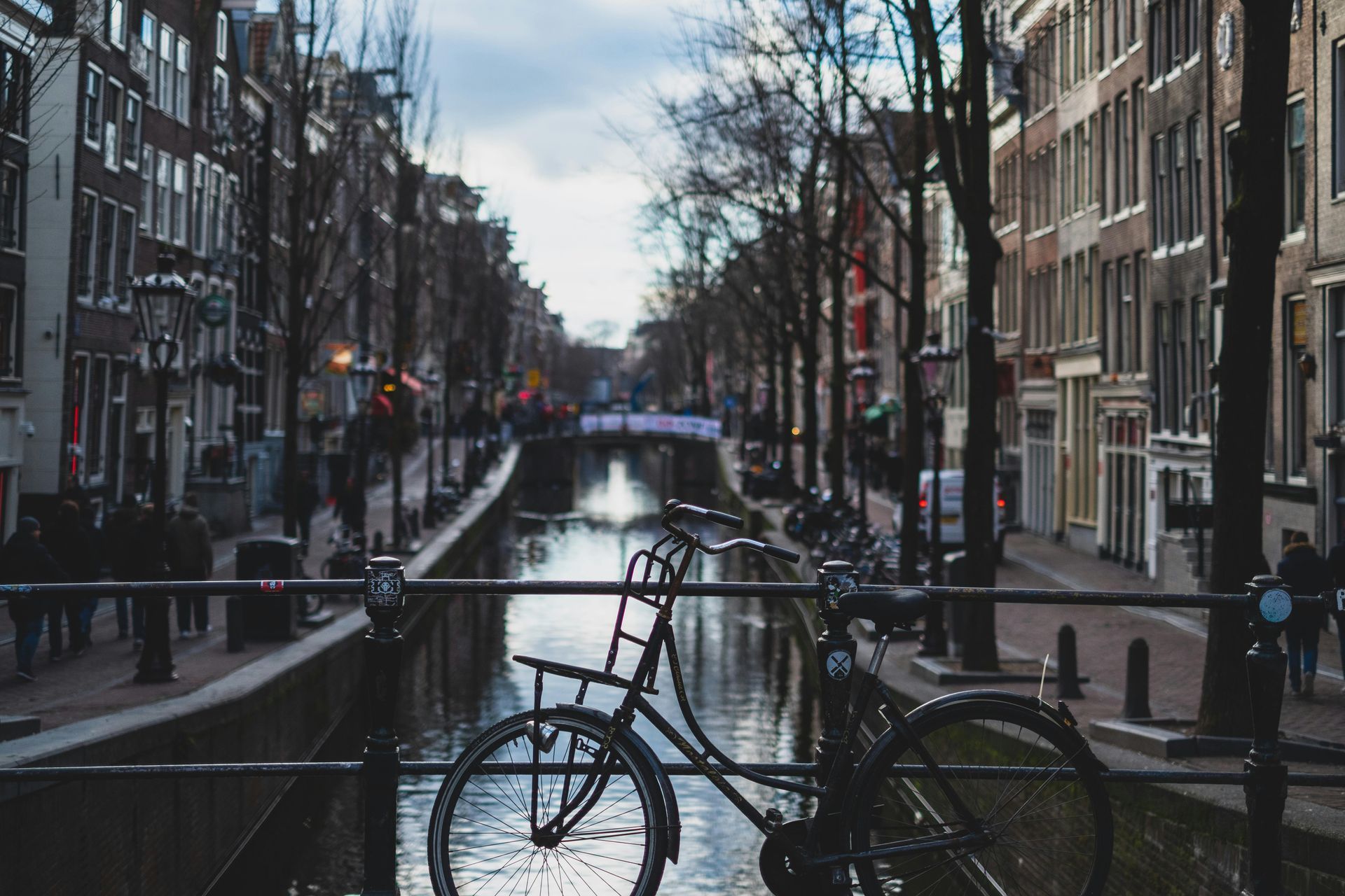 Canal in Amsterdam, Netherlands, with a bicycle parked on a bridge, lined by buildings and bare trees.