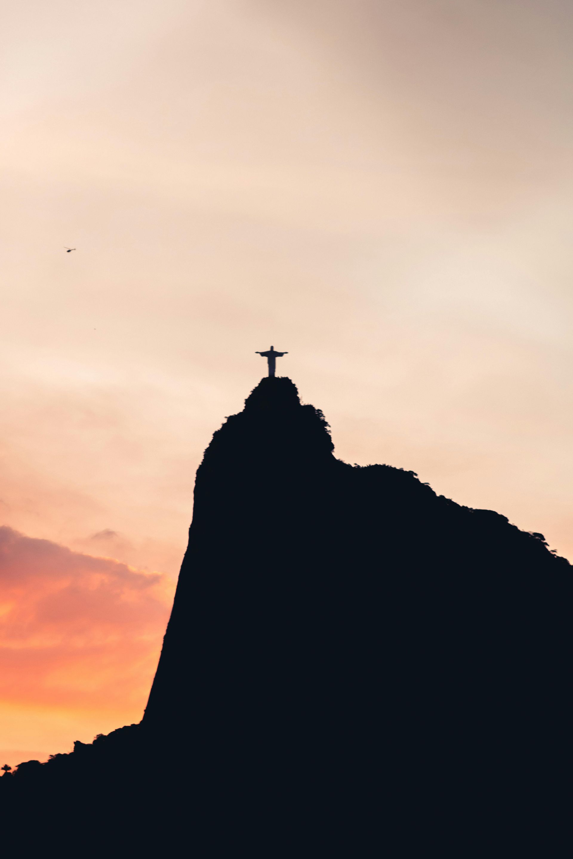 Silhouette of Christ the Redeemer statue on a mountain peak against a colorful sunset. Rio de Janeiro