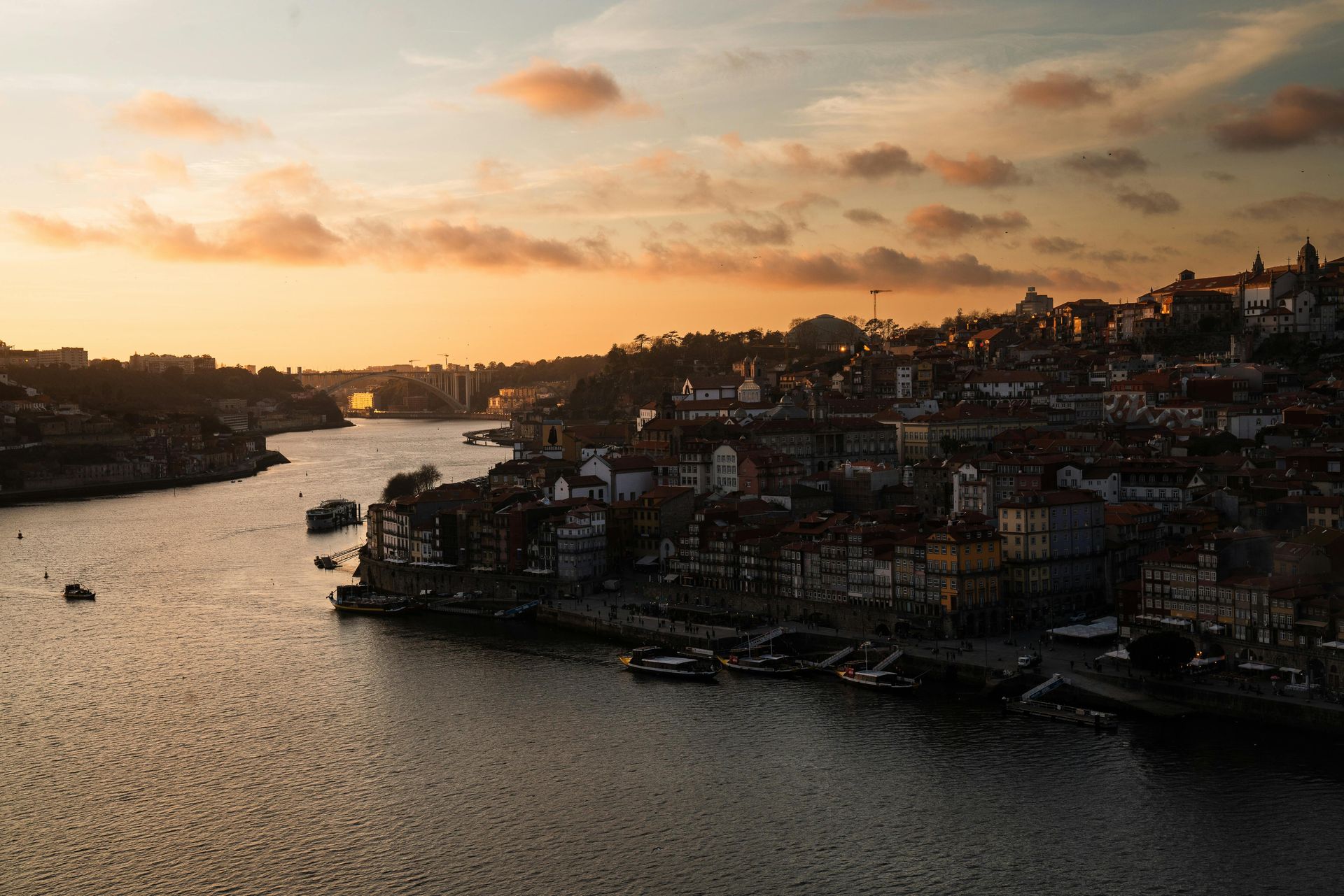A sunset view of a historic riverside city in Porto, Portugal, with warm light reflecting on the Douro River.