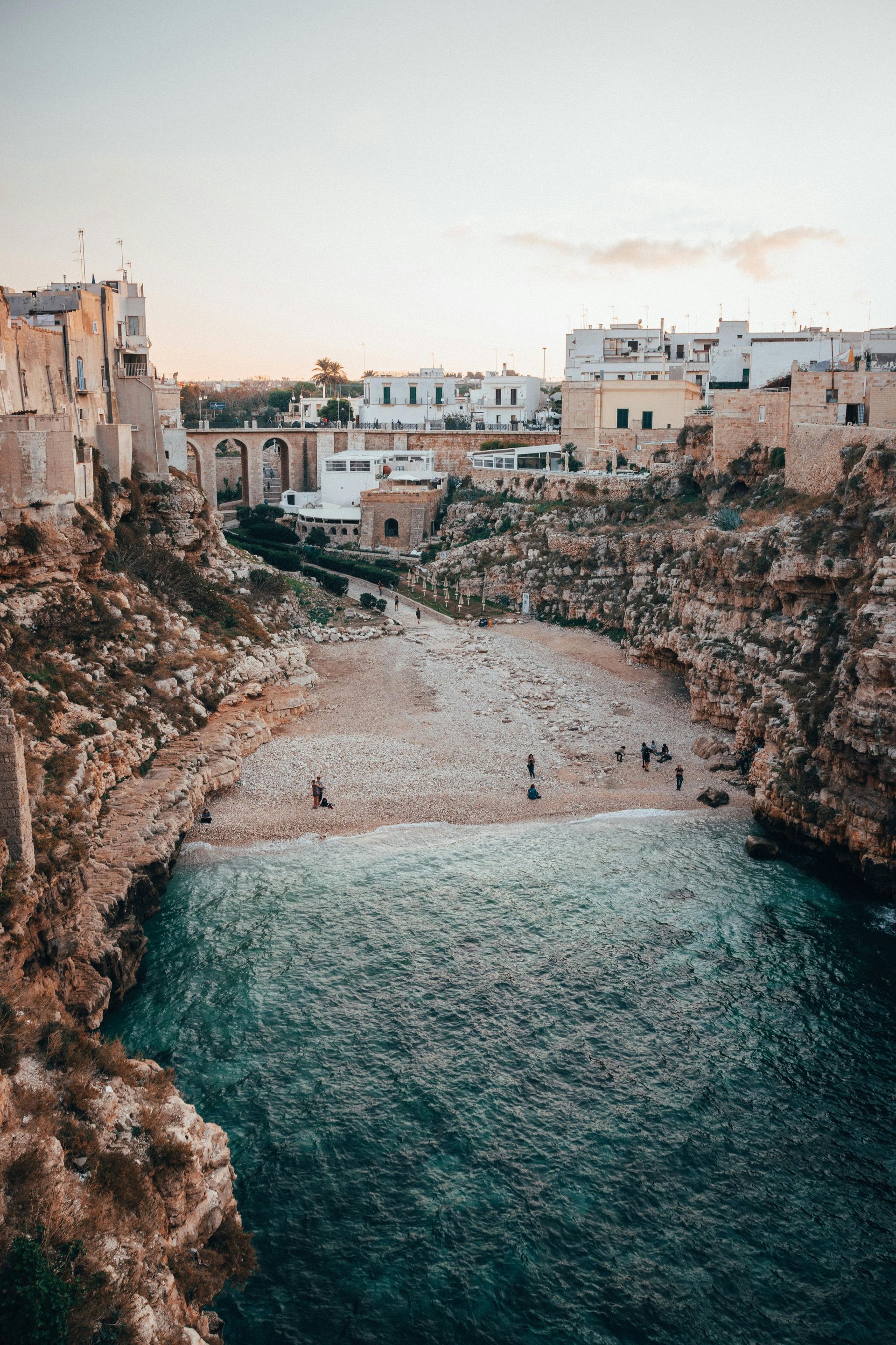 Coastal Italian town, buildings perched on cliffs, overlooking a pebbled beach and turquoise water. Polignano a Mare