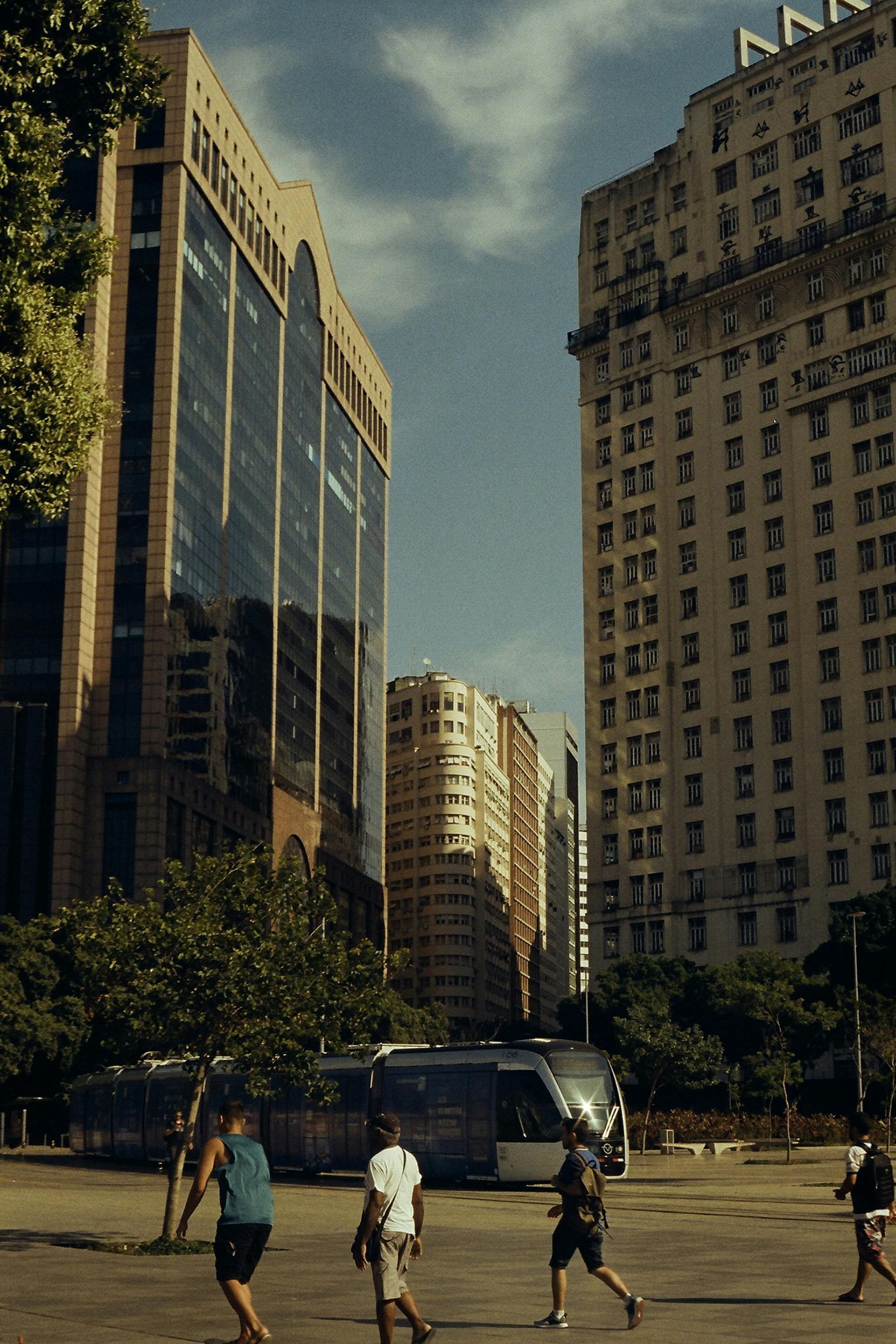 People crossing a street in front of tall buildings; bus and trees in view. Ipanema – Rio de Janeiro