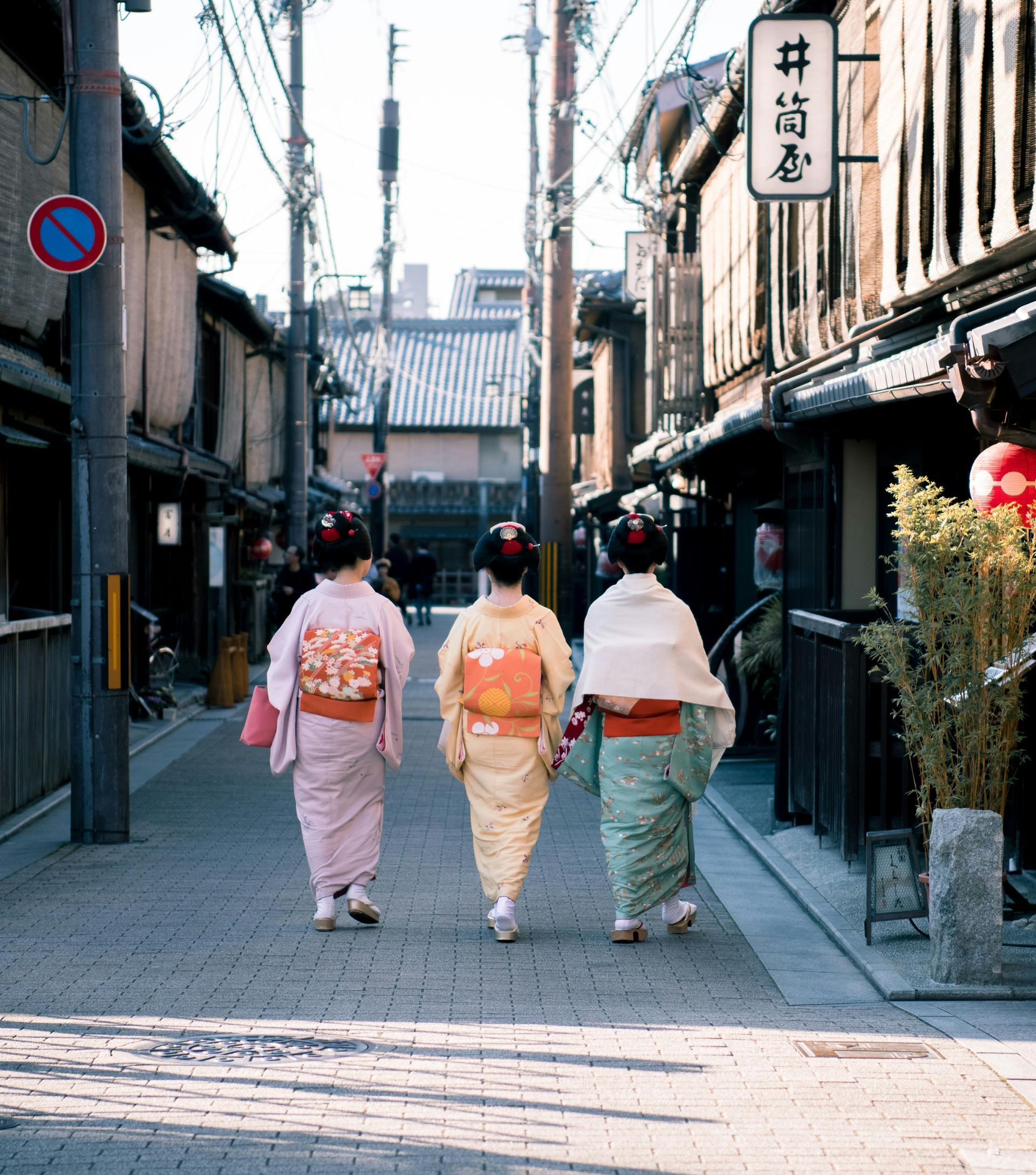 Three women in kimonos walking down a narrow street in Japan.