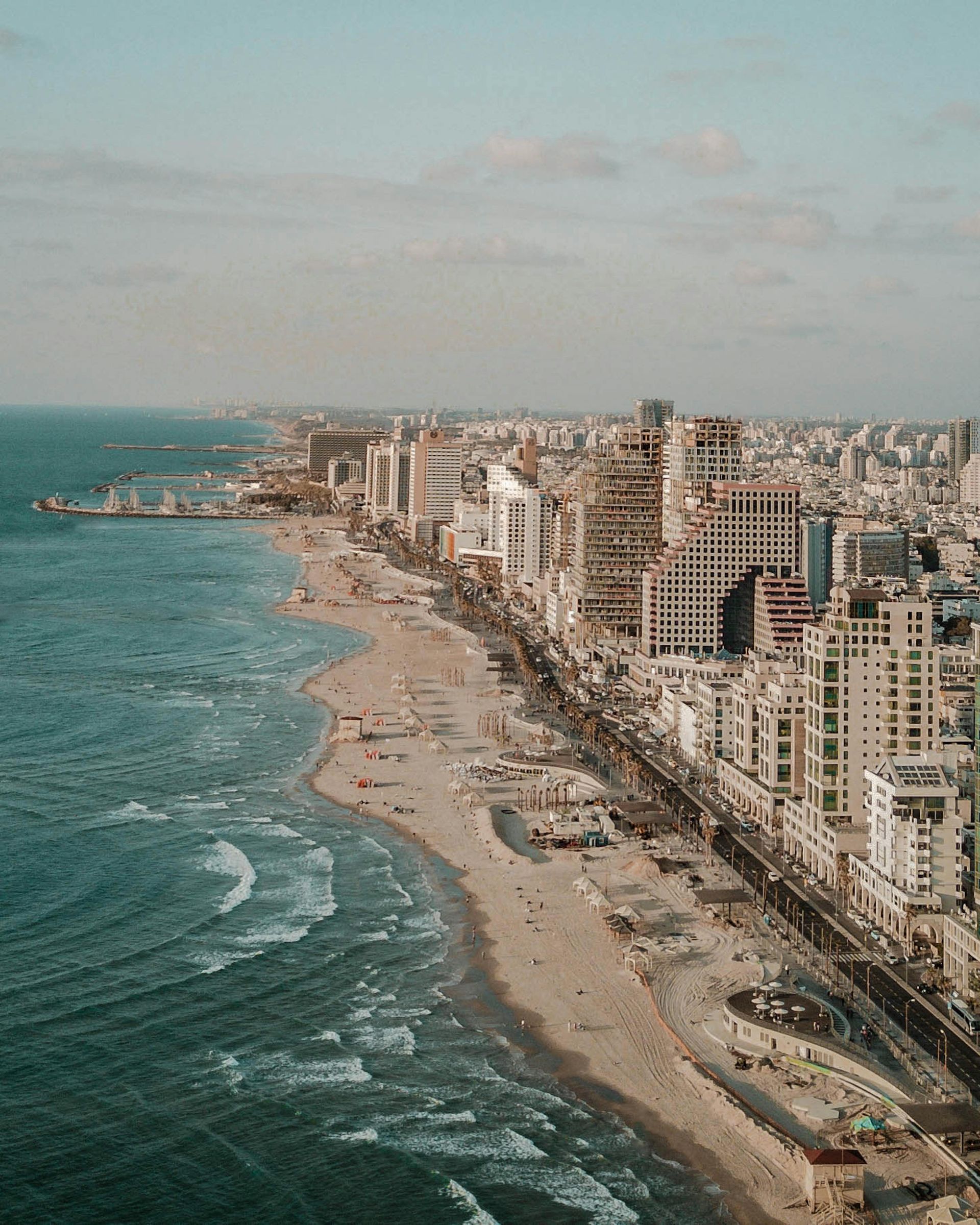 Coastal cityscape, beach with people, high-rise buildings, Tel Aviv, Israel, turquoise water, sunny.