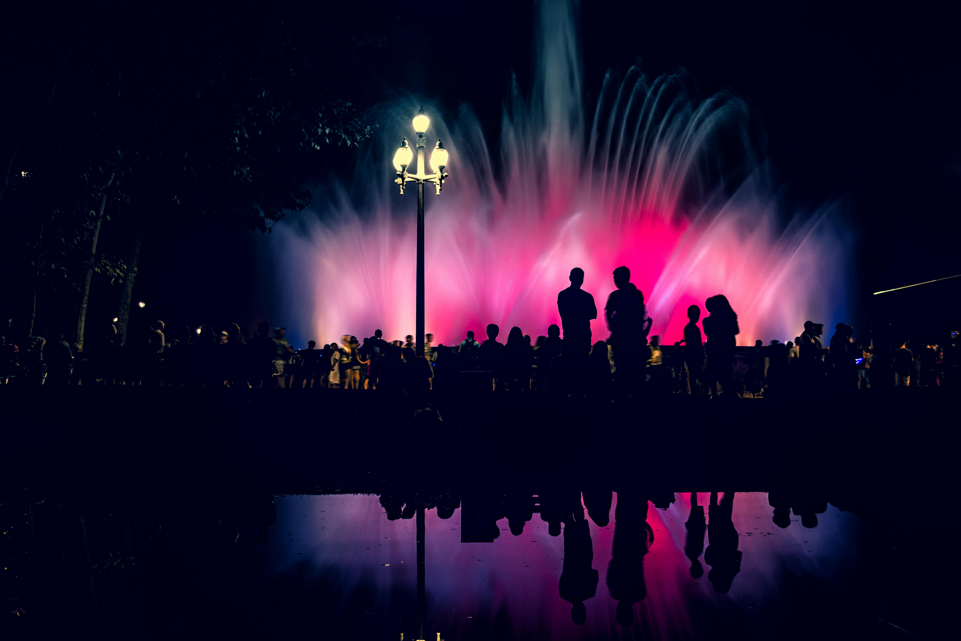 Nighttime fountain display with colorful lights and silhouetted spectators. Barcelona
