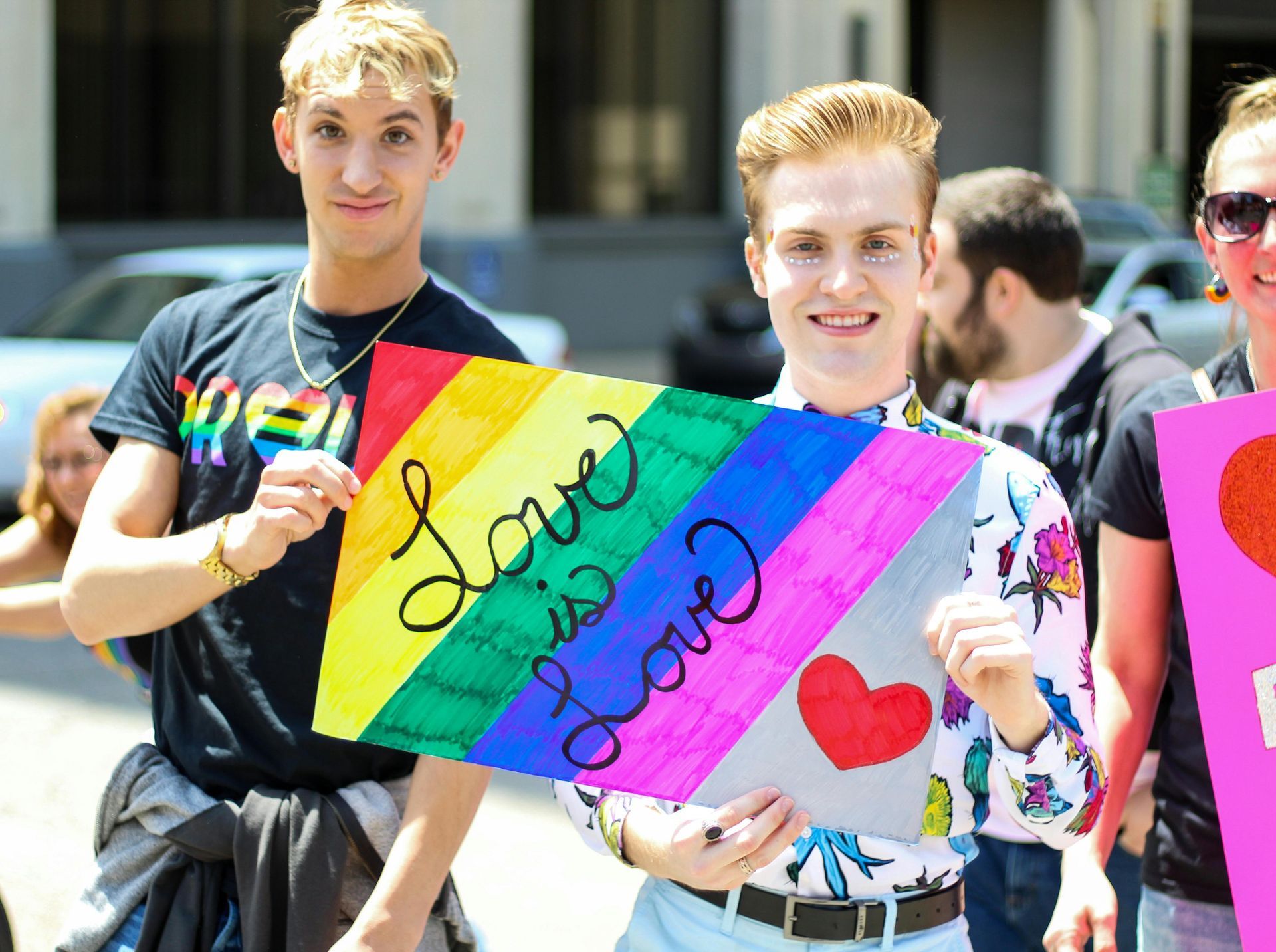Two smiling people hold a rainbow-striped sign that says