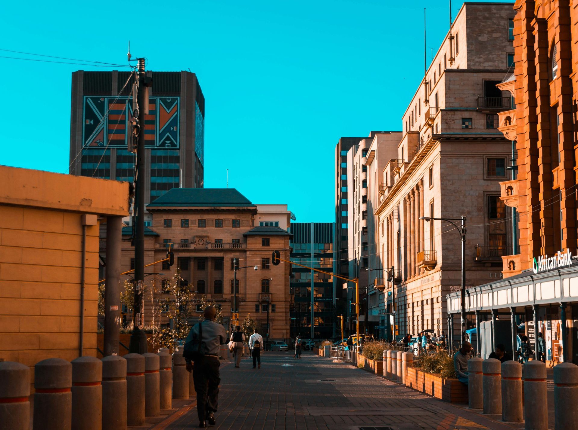 Street scene in a city with tall buildings, a person walking toward the camera on a paved path. Johannesburg