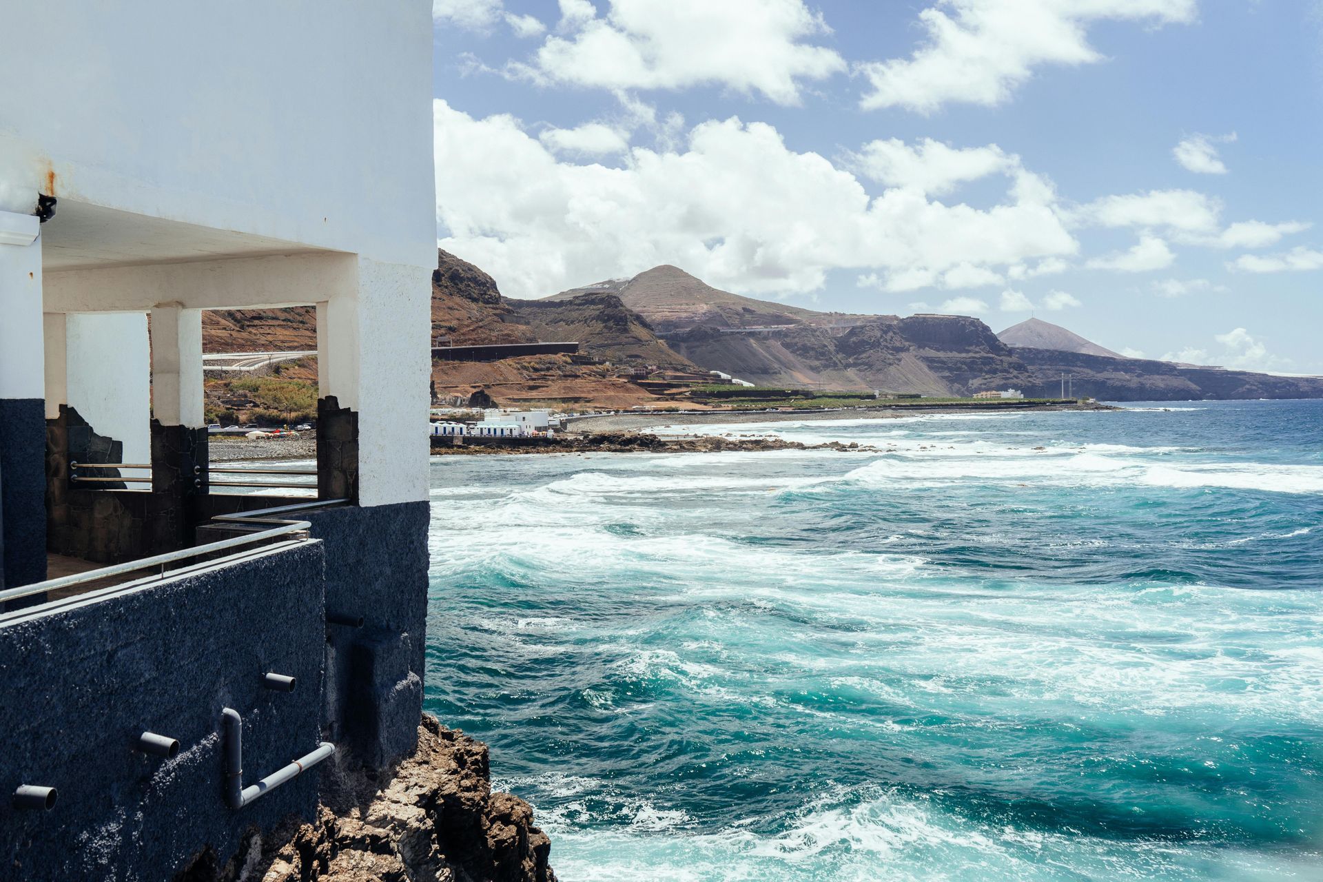 White buildings with blue domes in Santorini, Greece, under a bright blue sky with fluffy white clouds. Mykonos Gay