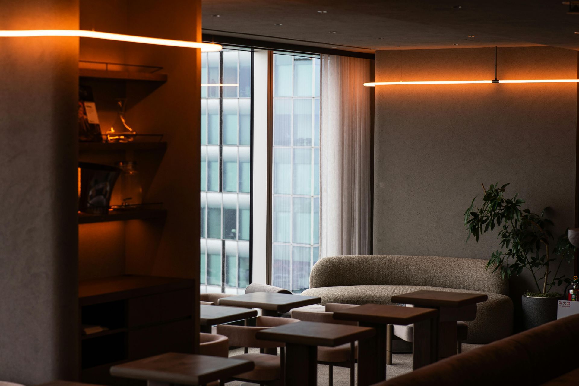 Interior view of a modern lounge with a sofa, tables, and a large window overlooking city buildings.
